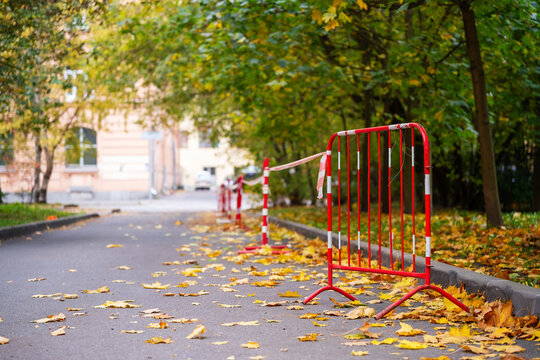 Red metal safety barriers lining autumn park path with fallen leaves, street construction fence