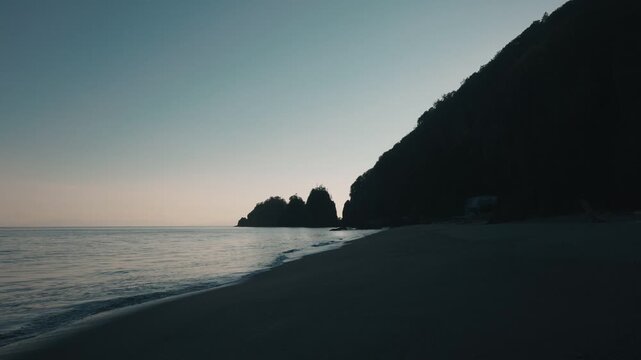 Gentle waves washing onto a quiet beach, with a beautifully gradient sky and the silhouette of coastal cliffs in the background