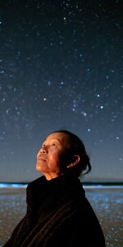 Older woman on a starlit beach at night looking up for reflective background and calm poster or banner design