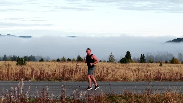 Drone cinematic tracking shot flying parallel from right to left with an athletic man jogging on a high altitude mountain road.