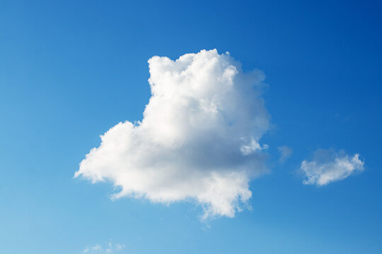 Large fluffy white cloud and small light cloud on bright blue cloudless sky on a sunny day with copy space