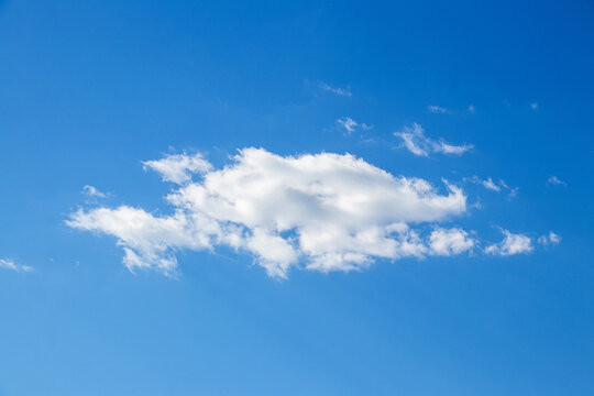 White fluffy elongated cloud and small light clouds on bright blue cloudless sky on a sunny day with copy space
