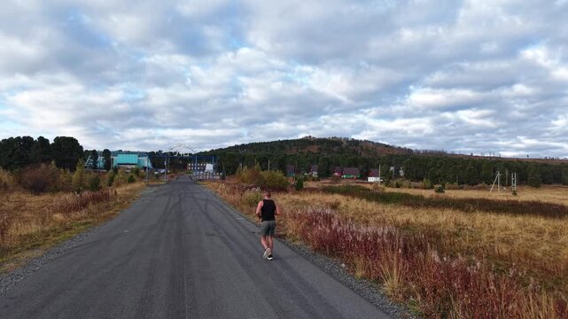 Back high angle view of a determined sportsman running on an asphalt road heading to a mountain training center.