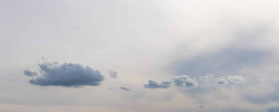 Small dark gray clouds on light overcast sky with soft pastel tones and copy space