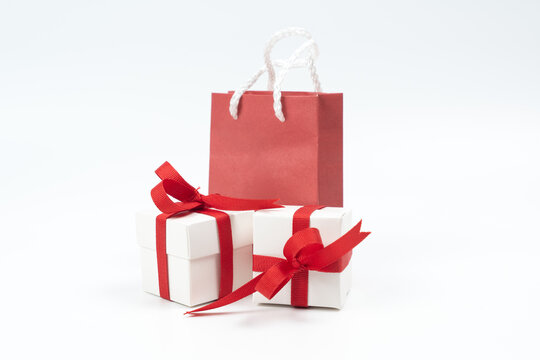 Small white wrapped gift boxes decorated with red ribbons alongside a red paper shopping bag. Perfect for Christmas sales, Valentine's Day, holidays, and promotional retail shopping concepts.