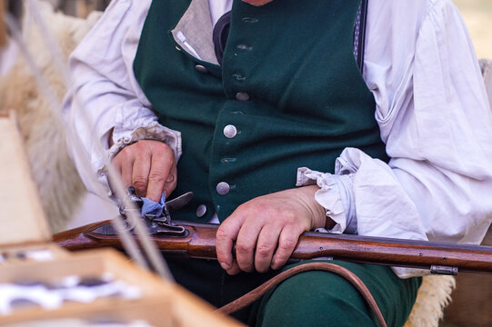 Reenactor cleaning a musket in early 19th century clothing. Close view of a reenactor in period clothing cleaning a musket at a historical reenactment camp.