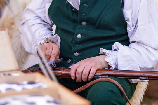 Reenactor with musket in early 19th century costume clothing. Close view of a reenactor in period clothing cleaning musket at a historical reenactment camp.