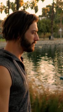 Athletic man jogs around a small lake in Los Angeles. Vertical video.