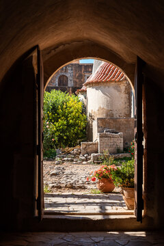 Arkadi, Greece - October 03, 2026 - Open Arched Wooden Gate View into Courtyard with Potted Flowers at Arkadi Monastery