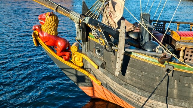 Red lion wooden figurehead on the bow of Libava ship, a historical 17th-century Dutch Herren yacht replica, on a blue sea background.