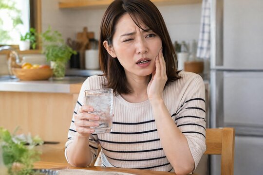 Woman wincing at cold drink sensitivity in a tooth at home in soft natural light