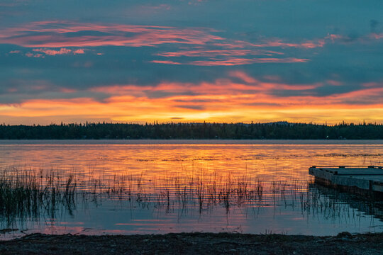 Orange sunset reflected in calm lake water with reeds and fishing pier