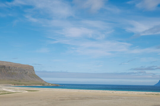 Wide sandy beach Brei&eth;av&iacute;k Beach, iceland and calm blue sea beneath a soft cloudy sky, framed by rugged coastal cliffs in a quiet natural landscape.