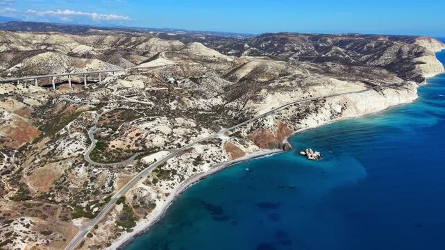 Aerial panoramic view of the scenic coastal road, highway bridge, and rugged rocky hills by the Mediterranean Sea near Petra tou Romiou, Cyprus.