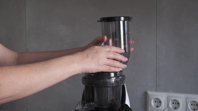 Woman hands installing a plastic lid hopper on a slow juicer machine, assembling a modern kitchen appliance for fresh juice