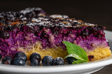 Piece of homemade blueberry pie closeup with fresh berries. Slice of delicious blueberry cake on white plate. Macro view of sweet berry tart with fresh blueberries and mint for bakery or cafe menu © OlegD