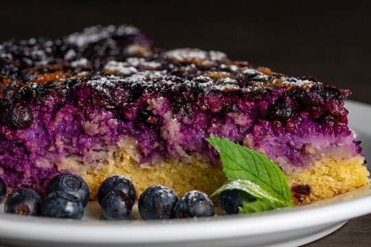 Piece of homemade blueberry pie closeup with fresh berries. Slice of delicious blueberry cake on white plate. Macro view of sweet berry tart with fresh blueberries and mint for bakery or cafe menu