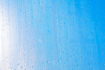 Fototapeta premium Water droplets bead across a glass surface, creating vertical trails and sparkling textures. Bright light gives the cool, abstract image a fresh, translucent appearance
