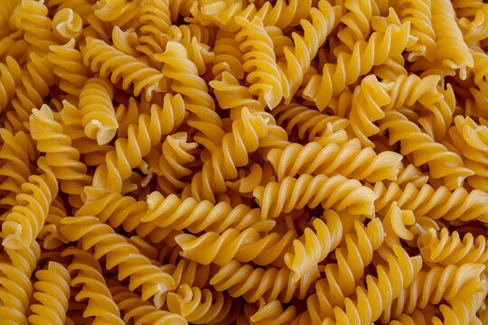 Close-up of uncooked fusilli pasta spirals filling frame with warm golden color, repetitive texture, 
