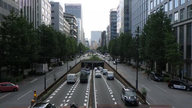 TOKYO, JAPAN - 20261003: Traffic flowing into a tunnel underpass surrounded by green street trees and modern office buildings.