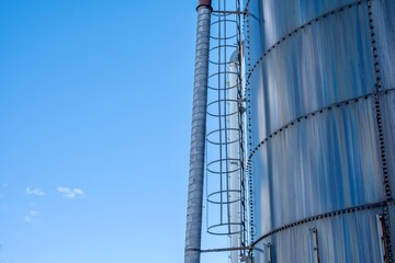 Metal silo ladder and pipe against blue sky © Maxwell