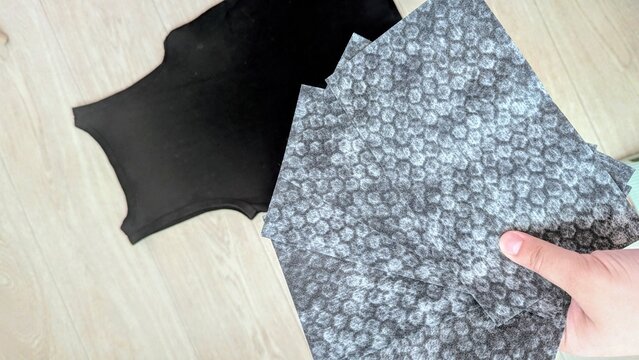 Hand holding black color-catching laundry sheets designed to transfer or intensify black color in clothing during washing. Top-view product concept on a light wooden surface.