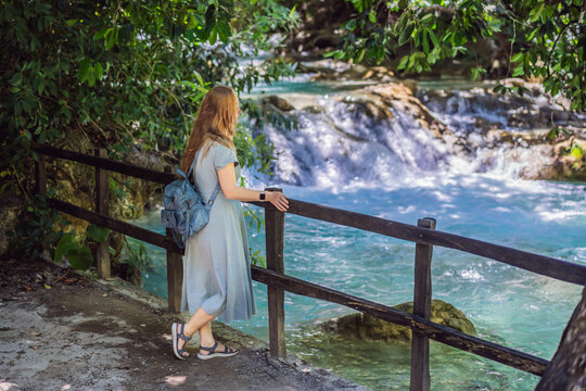 Woman traveler admiring El Chiflon waterfall from a wooden viewpoint in Chiapas Mexico with wooden railings tropical forest clear blue water nature travel and smiling.