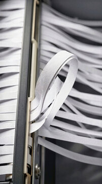 Close up of white paper strips from a document shredder. Curled ribbon detail with overlapping layers and vertical machine housing. Office equipment, data security and privacy protection concept