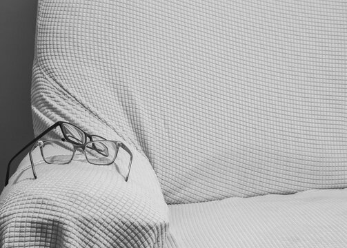 A Pair of Reading Glasses on the Arm of a Textured Fabric Sofa Chair.