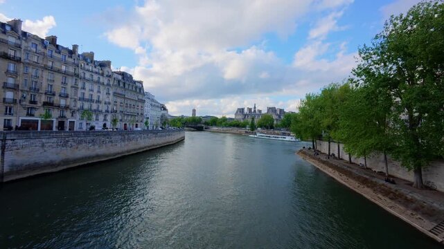 Wide view along the river Seine toward the Hotel de Ville with cream Haussmann buildings on the quay, a tree lined lower promenade with people relaxing and a tour boat, Paris, France