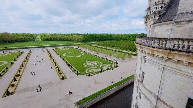 Formal French garden with fleur de lis lawn parterres, topiary cones and gravel paths beside the moat, static high view from a castle roof terrace, Chateau de Chambord, Loire Valley, France
