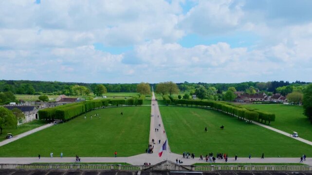 Long straight avenue between wide lawns and curved rows of clipped trees seen from the castle roof terrace with a French flag, visitors and horse riders, Chateau de Chambord, Loire Valley, France