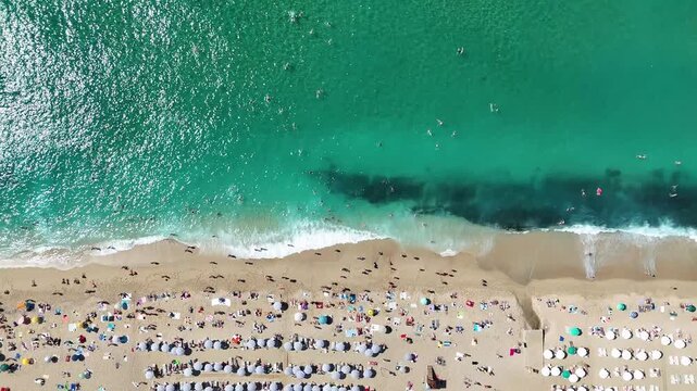 4K top down aerial drone video of crowded public beach, colorful umbrellas and turquoise sea waves in Alanya, Antalya, Turkey. Bird eye view of summer vacation, tourists, sandy shore and coast.