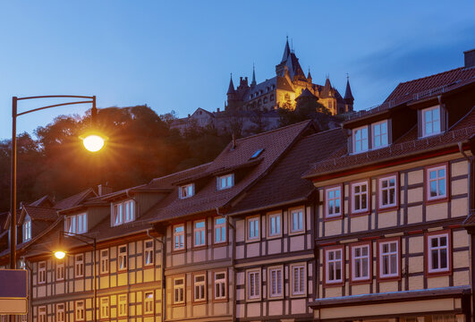 Illuminated historic architecture above traditional half-timbered houses during blue hour in Wernigerode, Germany.