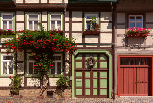 Colorful traditional half-timbered houses with decorative facades, red tiled roofs and flowers along a cobblestone street in Wernigerode, Germany.