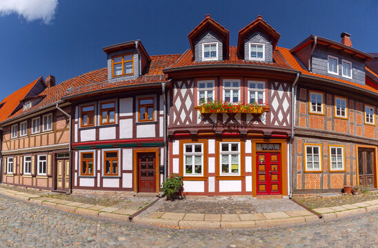 Colorful traditional half-timbered houses with decorative facades, red tiled roofs and flowers along a cobblestone street in Wernigerode, Germany.