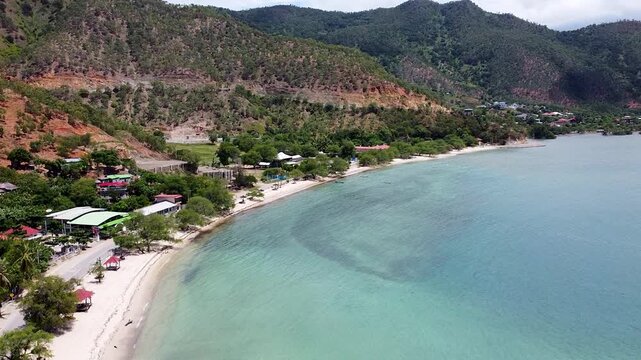 Aerial view rising over Dili Timor-Leste with white sand beach, turquoise ocean and rugged hill terrain in Southeast Asia