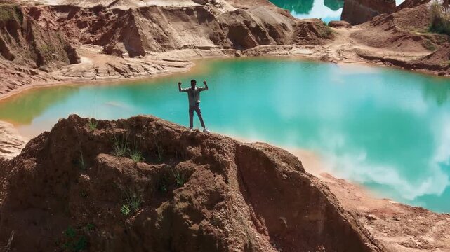 Man with arms outstretched above a turquoise quarry lake