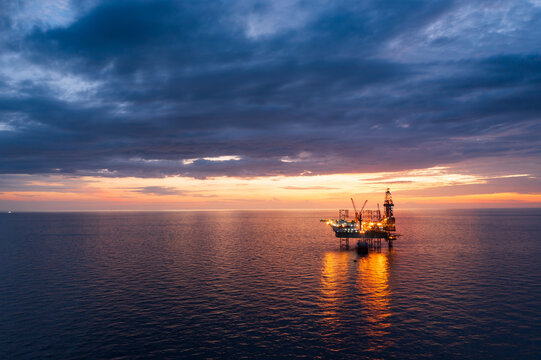 Aerial view from a drone of big jack up offshore drilling oil rig, production platform and supply vessel In the ocean during sunset - Oil and Gas Industry