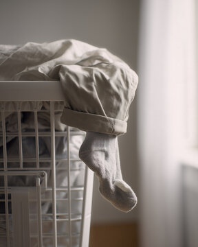 Humorous close-up editorial photograph of trousers draped over a laundry basket with one lonely sock trapped inside, ideal for laundry, household, cleaning & relatable lifestyle content.
