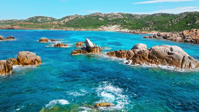 Drone view of Bassa Trinita Beach in La Maddalena. Rocky formations, shallow blue water and island coastline create a peaceful Sardinian beach landscape.