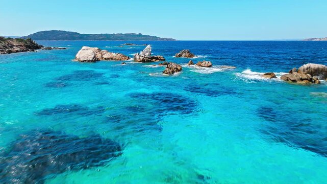 Aerial view of Bassa Trinita Beach in Sardinia. Granite rocks, clear turquoise water and distant coastline create a scenic Mediterranean seascape.
