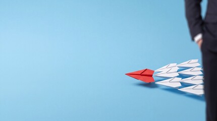 Fototapeta premium Red Paper Plane Leading a Group of White Ones Representing Business Leadership and Vision with Large Negative Space for Text on a Blue Background beside a Professional Businessman