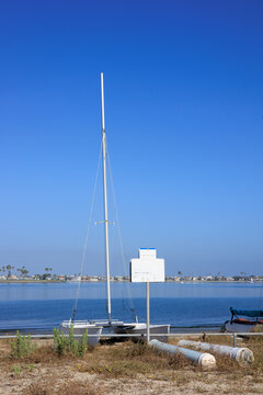 White catamaran sailboat with a tall mast sits on the shore of Mission Bay under a clear blue sky, San Diego, California