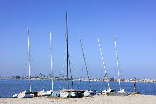Boat beaching area lined up with small catamaran sailboats on the shore of Sail Bay in San Diego under a California blue sky