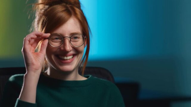 Young Red-Haired Woman Laughing and Adjusting Her Glasses in Office