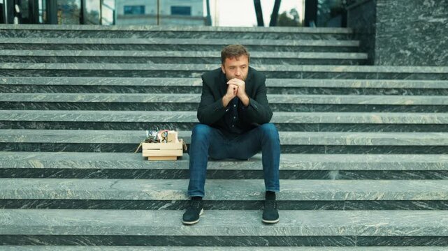 Laid off corporate specialist after staff reduction leaning forward on stairs covering face in hands. Workplace trauma and grief
