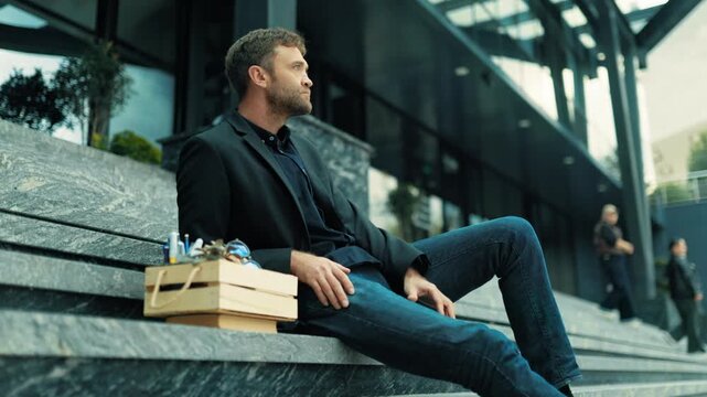 Jobless male professional leaning back on corporate stairs near office box. Unpaid bills and debt