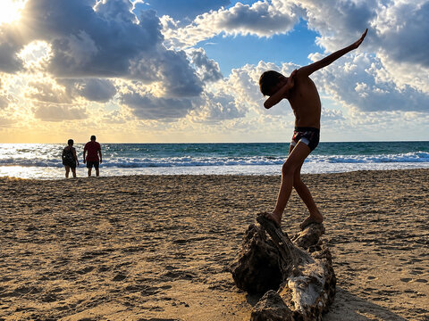 Boy posing on driftwood at sunset on a tropical beach in Zihuatanejo Mexico