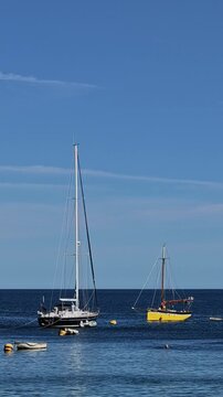 Polperro Cornwall England UK. 20.08.2026. Video. Small yellow yacht under power approaching moorings  off Polperro harbour against a blue summer sky.